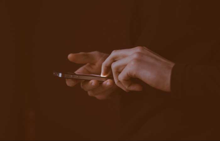 Close-up of hands holding and using a smartphone against a dark background.
