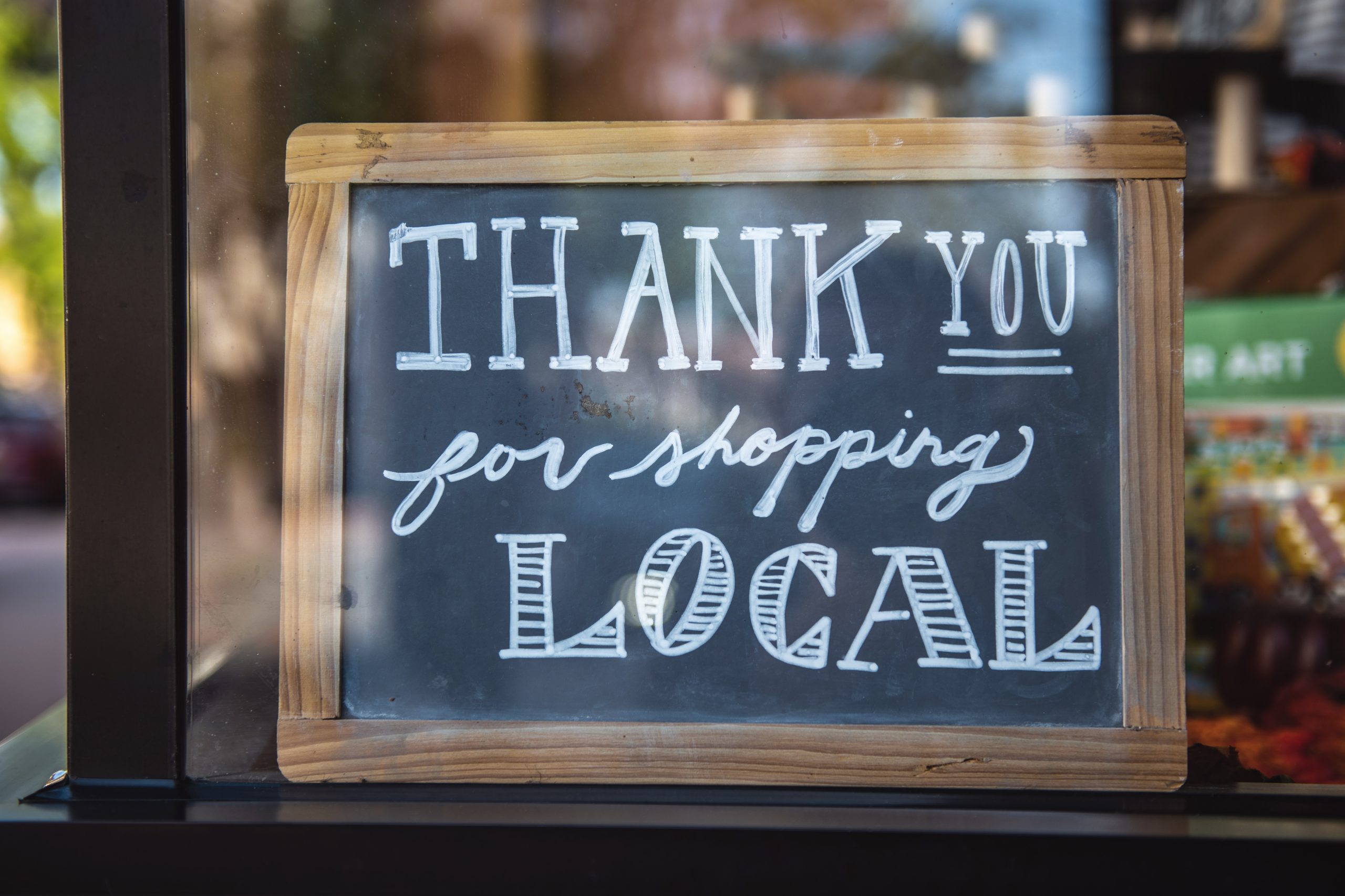Chalkboard sign reads “Thank you for shopping local” on display in a store window.