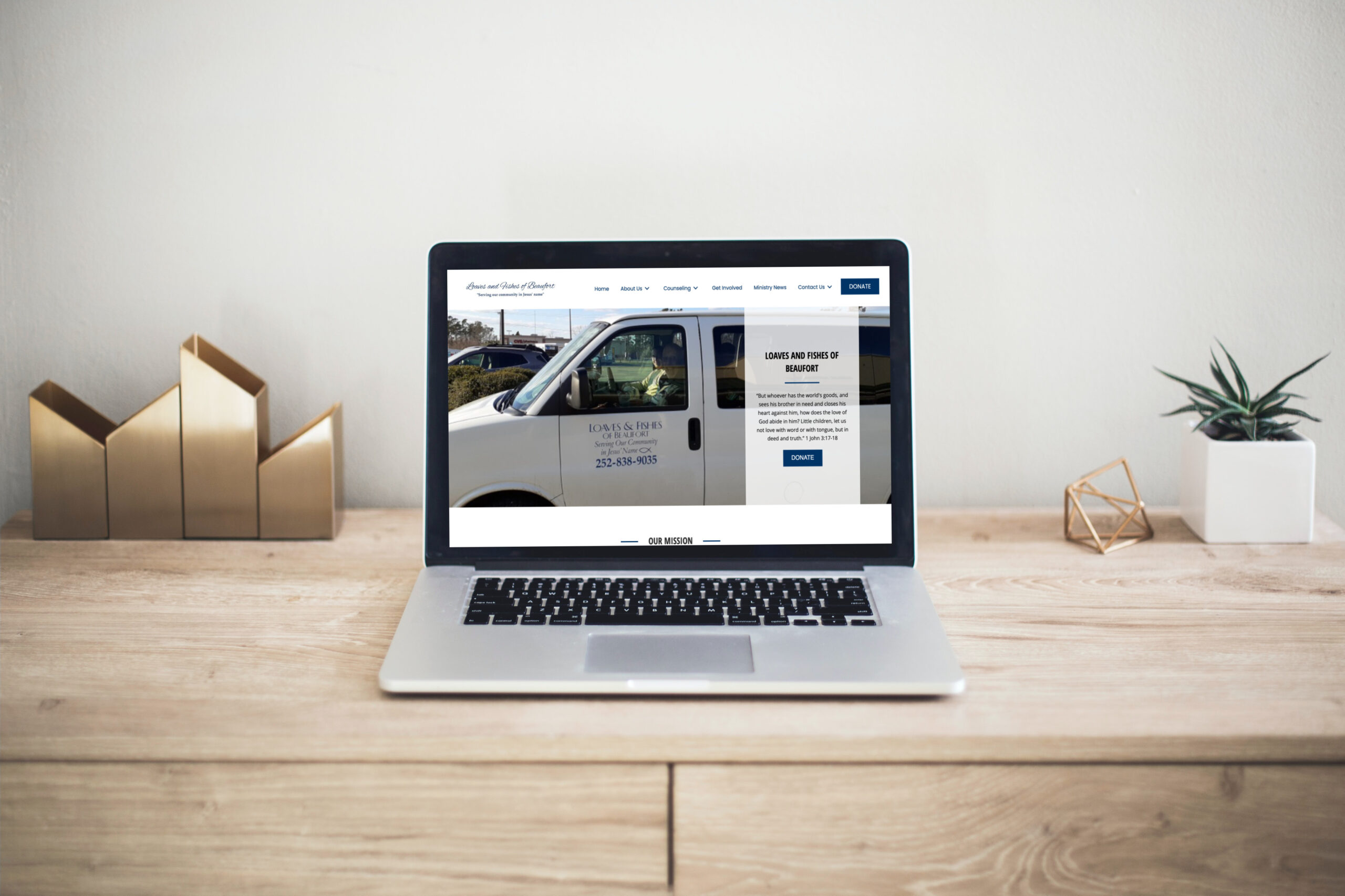 A laptop on a wooden desk displays a website featuring a white van and contact information.