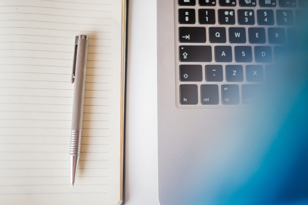 A silver pen on a lined notebook next to a laptop keyboard, with a blue blur on the right side.