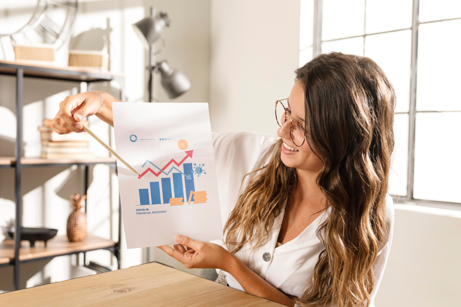 Smiling woman pointing at an ROI financial recovery chart in an office with sunlight streaming through the window.