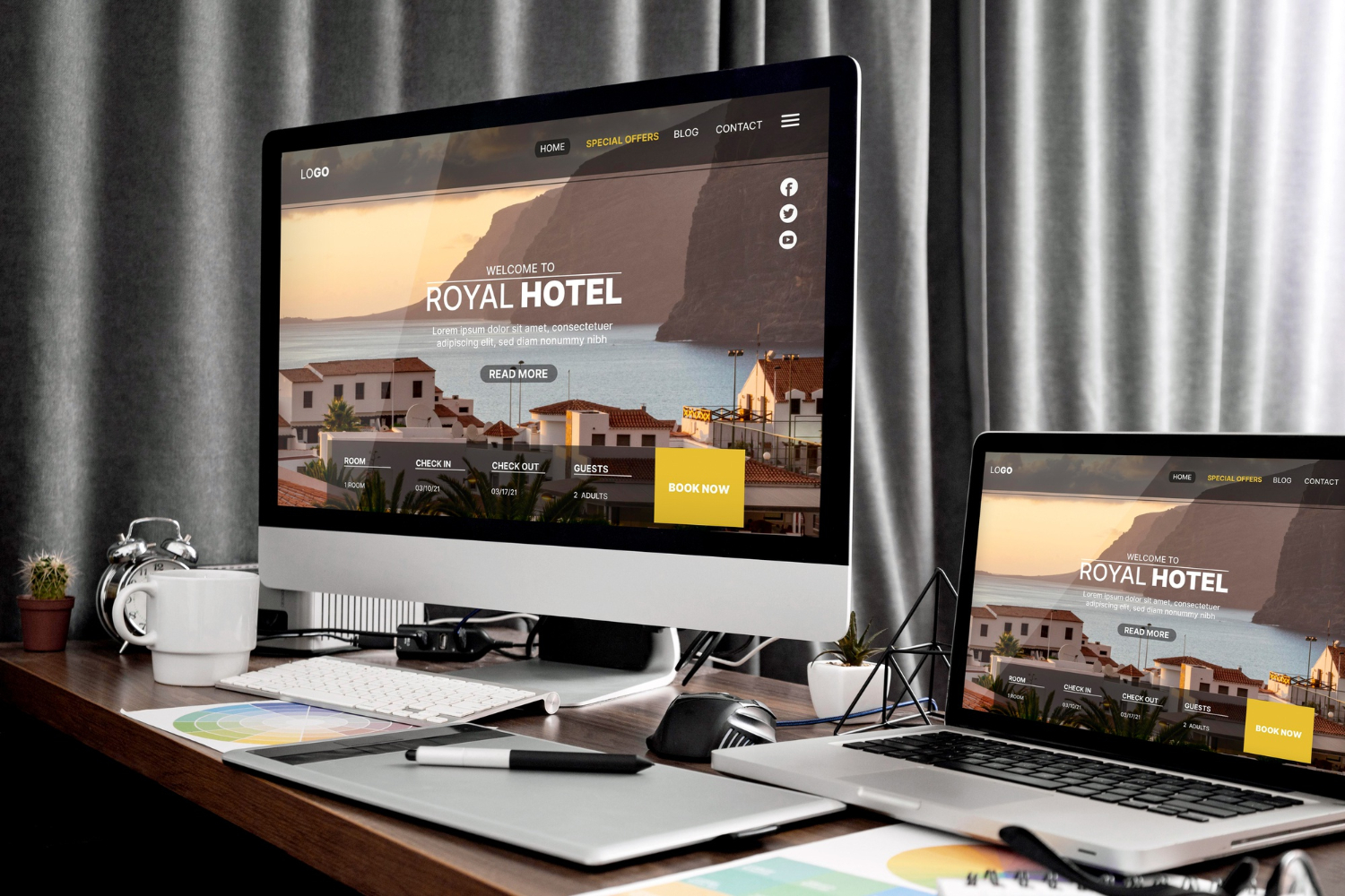 Desktop and laptop on a desk display a hotel booking website with a scenic coastal village image.